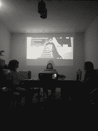 People seated around a table in front of the projection of the work in a dark room